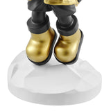 Close-up view of the feet of a golden astronaut sculpture standing on a white, faceted base. The astronaut is wearing gold boots with black soles.